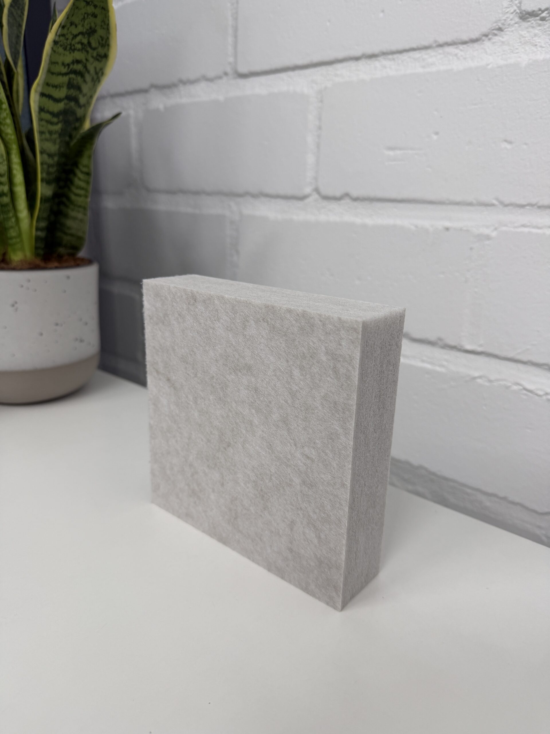 Detailansicht der Faserstruktur eines Schallschluck-Materials zur Reduzierung von Hall, stehend vor einer weißen Backsteinwand.